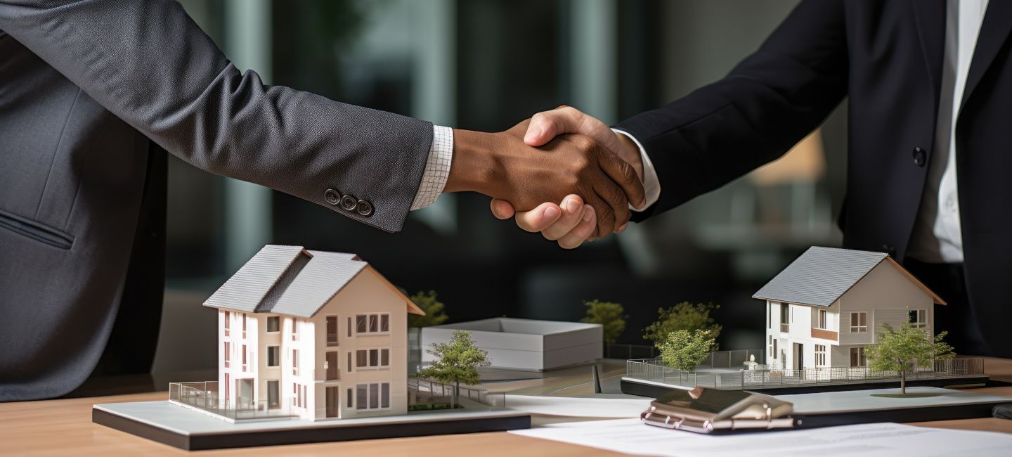 Handshake between two people and two models of a detached house and an apartment building in the foreground